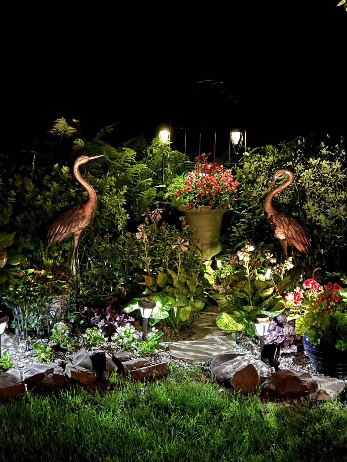 A lit garden at night with two heron sculptures